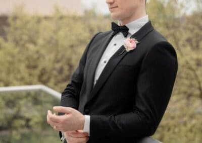 Groom in formal black tuxedo with bow tie and pink boutonniere for wedding photos.