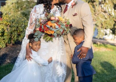 Romantic outdoor wedding at Zolana Weddings with a happy newlywed couple, children, and lush garden backdrop.
