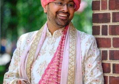 Elegant groom wearing pink turban with gold jewelry and embroidery.