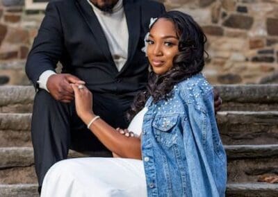 Beautiful wedding couple sitting outdoors with rustic stone background, showcasing elegant wedding photography.