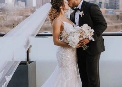 Bride and groom share romantic moment on rooftop with city skyline backdrop, celebrating love and wedding day.