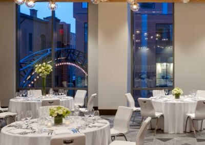 Stylish wedding reception with round tables, white linens, floral centerpieces, and modern lighting in a trendy venue.